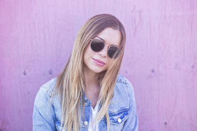 Portrait of young woman wearing sunglasses standing against wall