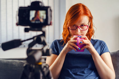 Portrait of woman holding camera while sitting at home