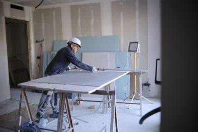 Construction worker measuring sheetrock on workbench at site