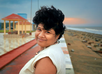 Portrait of smiling woman standing at beach against sky during sunset