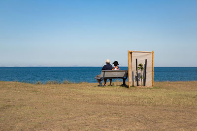 Men sitting on beach against clear sky