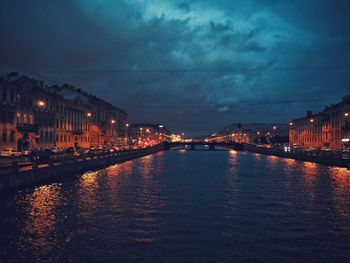 Illuminated buildings by river against sky at night