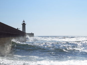 Lighthouse by sea against clear sky with fisherman and waves