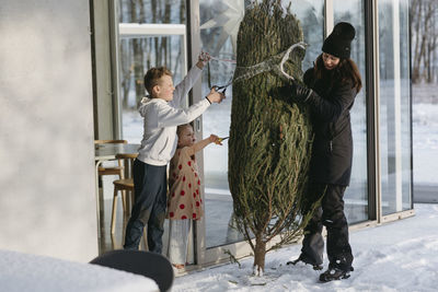 Woman with children preparing christmas tree in front of house