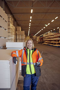 Portrait of happy blue-collar worker in protective workwear leaning on planks in distribution warehouse