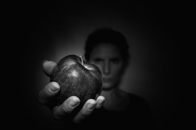Close-up of hand holding fruit against black background