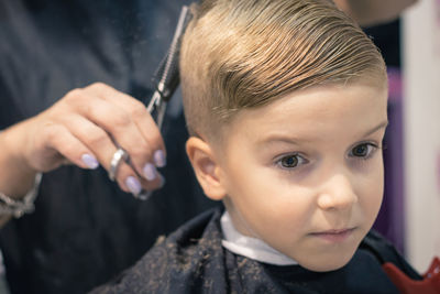 Midsection of female hairdresser styling boy hair in salon