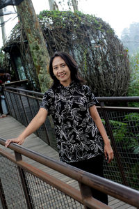 Portrait of smiling young woman standing on footbridge