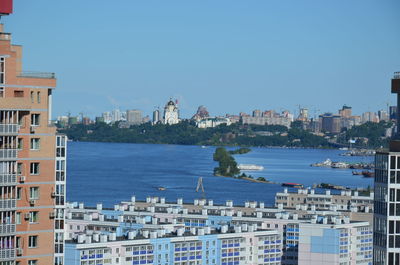 Buildings by sea against clear blue sky