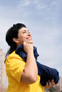 Young woman looking away while standing against sky