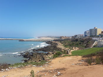 Scenic view of sea by buildings against clear blue sky