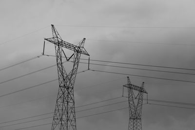 Low angle view of silhouette electricity pylon against cloudy sky