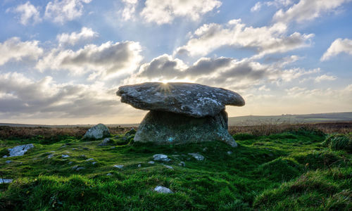 Rock on field against sky during sunset