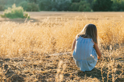 Rear view of girl crouching on grassy field in forest