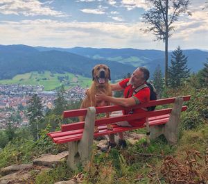 Woman with dog sitting on bench by mountains against sky