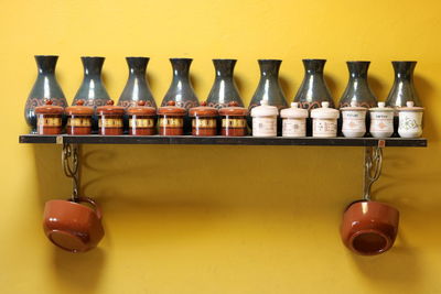 Jars and vases on shelf against yellow wall