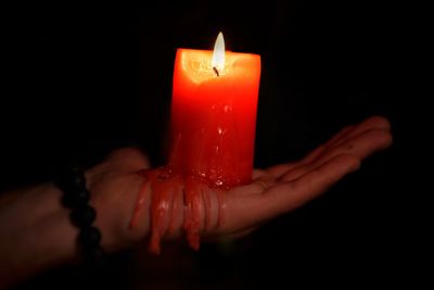 Close-up of hand holding illuminated candle against black background