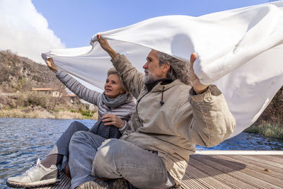 Couple holding blanket while sitting on pier