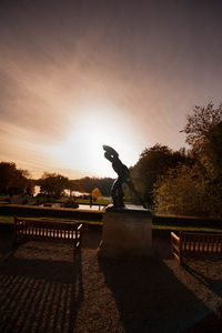 Statue of silhouette trees in city against sky