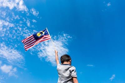 Low angle view of boy flag against blue sky