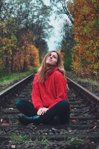 Young woman sitting on street amidst trees in forest