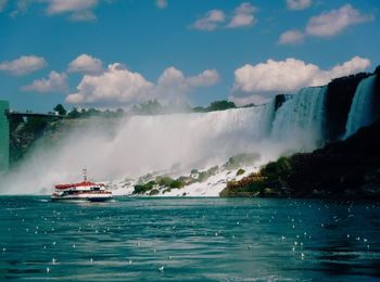 Boat by waterfall in river against sky during sunny day