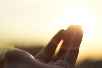 Cropped image of woman hand against sun shining in sky