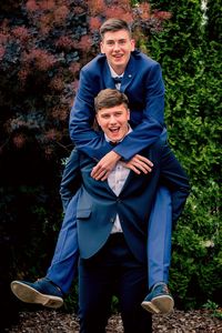 Portrait of cheerful man piggybacking male friend against plants