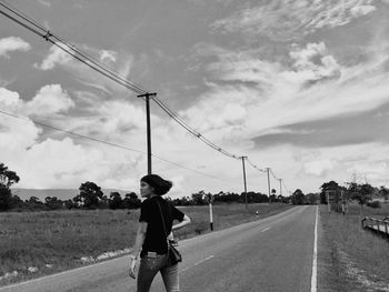 Rear view of woman standing on road against cloudy sky