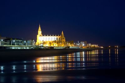 Illuminated church by beach against clear sky at chipiona