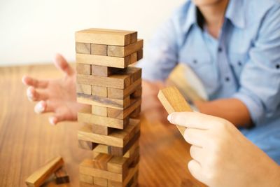 Cropped image of woman stacking dominoes while man trying to help on table