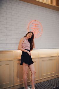 Portrait of smiling young woman standing against wall