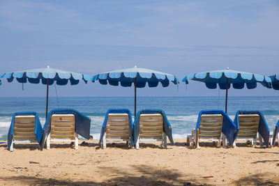 Lounge chairs and parasols at beach against sky