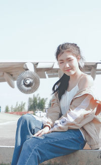 Portrait of smiling young woman sitting against sky