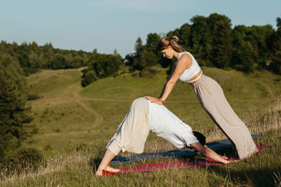 Young adult couple, man and woman practicing yoga outdoors with scenic landscape on the background	