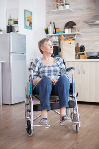 Full length of disabled woman sitting on wheelchair over floor