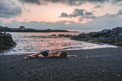 Rear view of woman lying on beach against sky