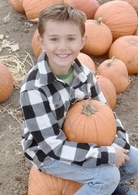 Portrait boy holding pumpkin while sitting on field