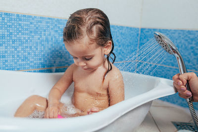 Cropped hand of mother showering girl in bathtub