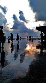 Silhouette people on beach against sky during sunset