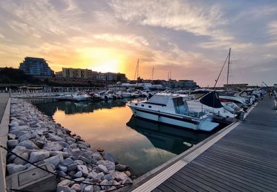 Sailboats moored at harbor against sky during sunset