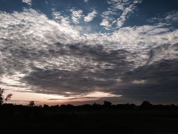 Silhouette trees on field against dramatic sky