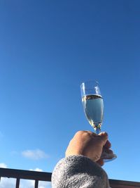 Midsection of man holding beer glass against blue sky