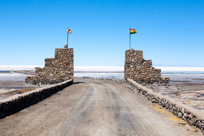 Road leading towards beach against clear blue sky