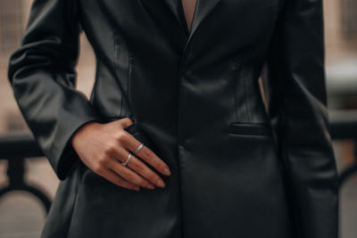 Fashion details of a black leather jacket with pockets and female hands with silver rings