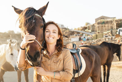 Portrait of smiling woman standing by horse against clear sky