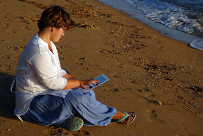Full length of woman using digital tablet while sitting at beach