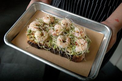 Hands holding a high angle view of open faced shrimp sandwich in tray