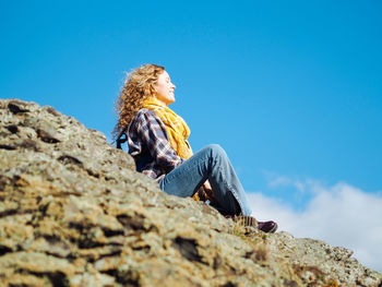 Young curly woman traveller in yoga pose doin meditation on a hill in autumn forest