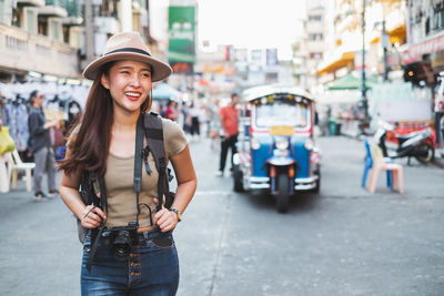 Portrait of smiling young woman standing on street in city